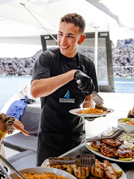 Guests being served food on a catamaran cruise with views of the sea in the background.