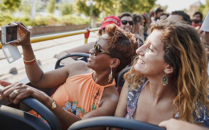 Tourists on a Milan Hop-On Hop-Off bus taking photos, enjoying city landmarks.