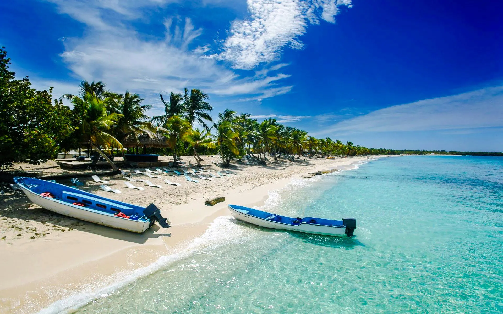 Boats on the sandy shore of Saona Island beach with palm trees and clear blue water.