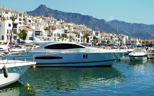 Yachts docked at Puerto Banús marina with mountains in the background.
