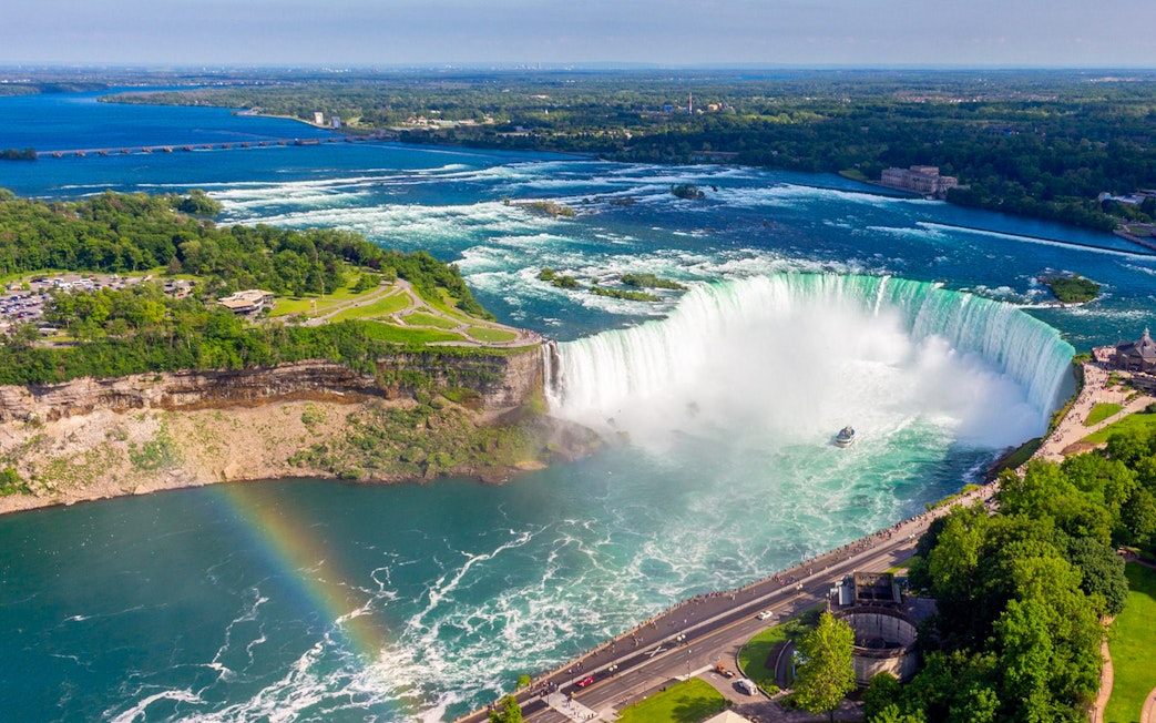 Aerial view of Niagara Falls with a rainbow and tour boat below.
