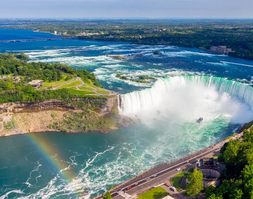 Aerial view of Niagara Falls with a rainbow and tour boat below.
