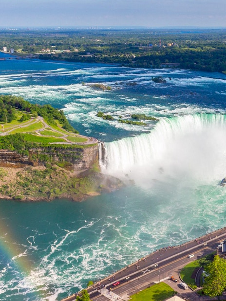 Aerial view of Niagara Falls with a rainbow and tour boat below.