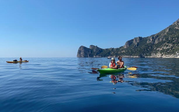 Kayakers exploring Ieranto Bay with rocky cliffs in the background.