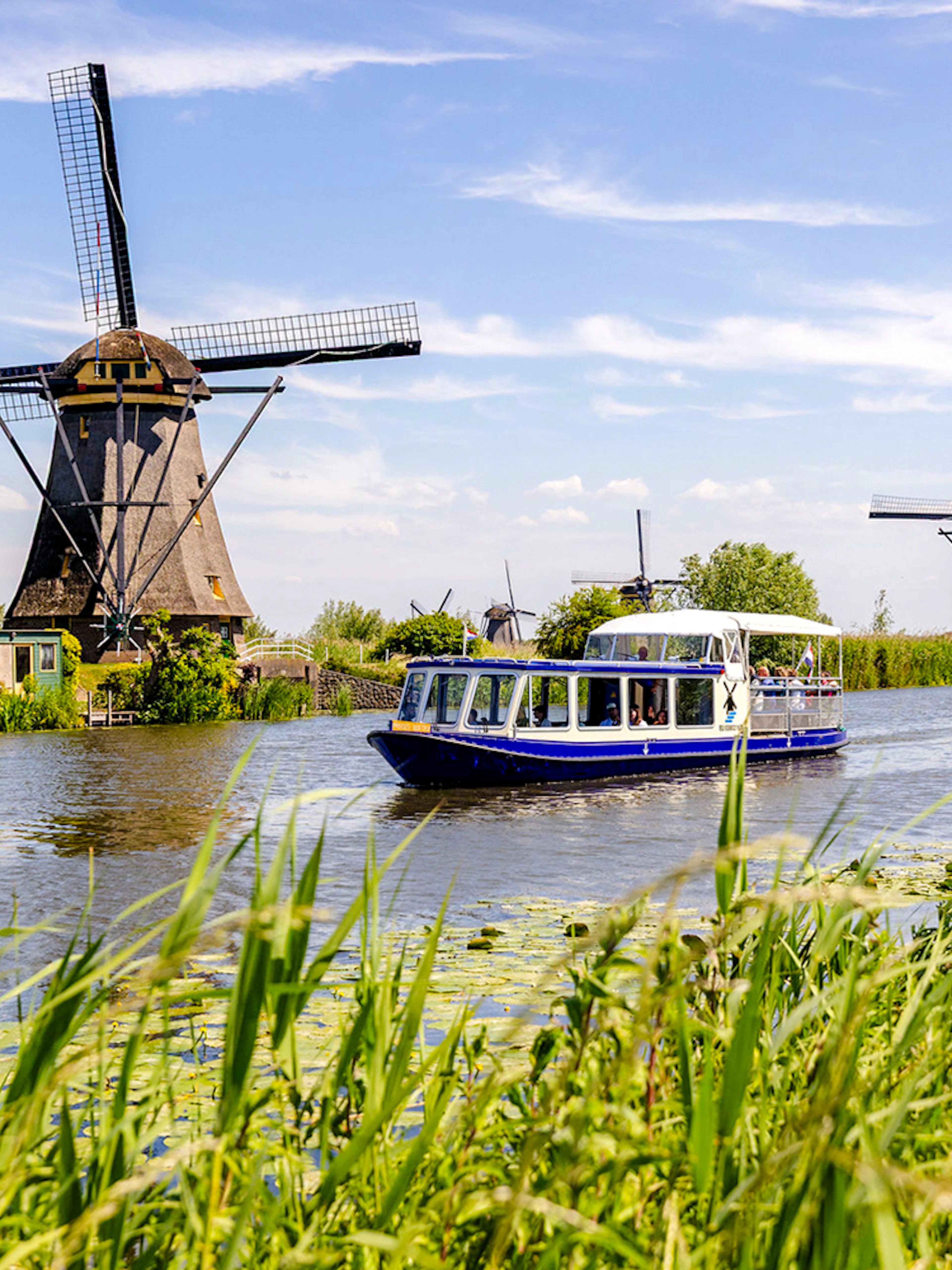 Tourist boat on Kinderdijk canal with historic windmills in the background.