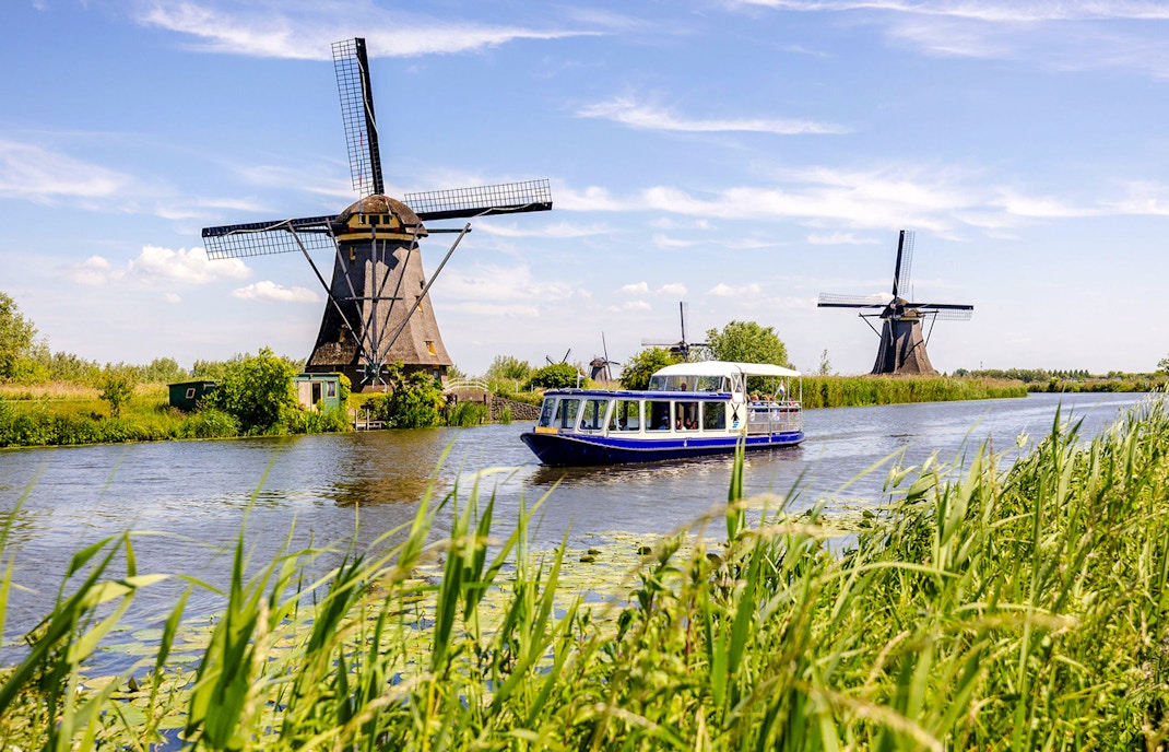 Tourist boat on Kinderdijk canal with historic windmills in the background.