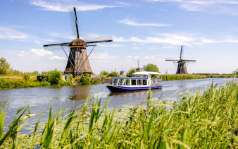 Tourist boat on Kinderdijk canal with historic windmills in the background.