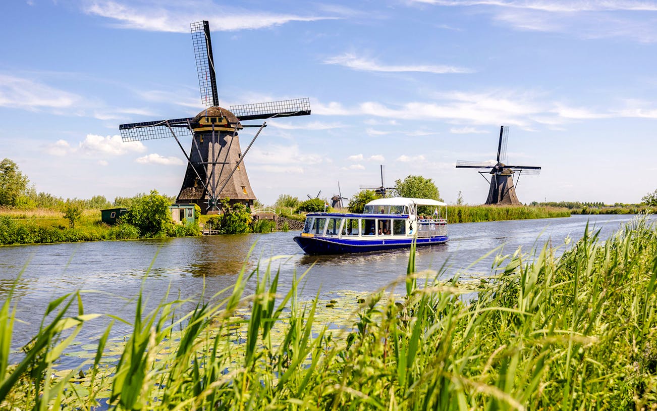 Tourist boat on Kinderdijk canal with historic windmills in the background.