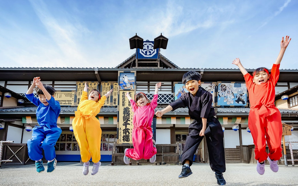 Tourists in colorful costumes jumping at Toei Kyoto Studio Park.