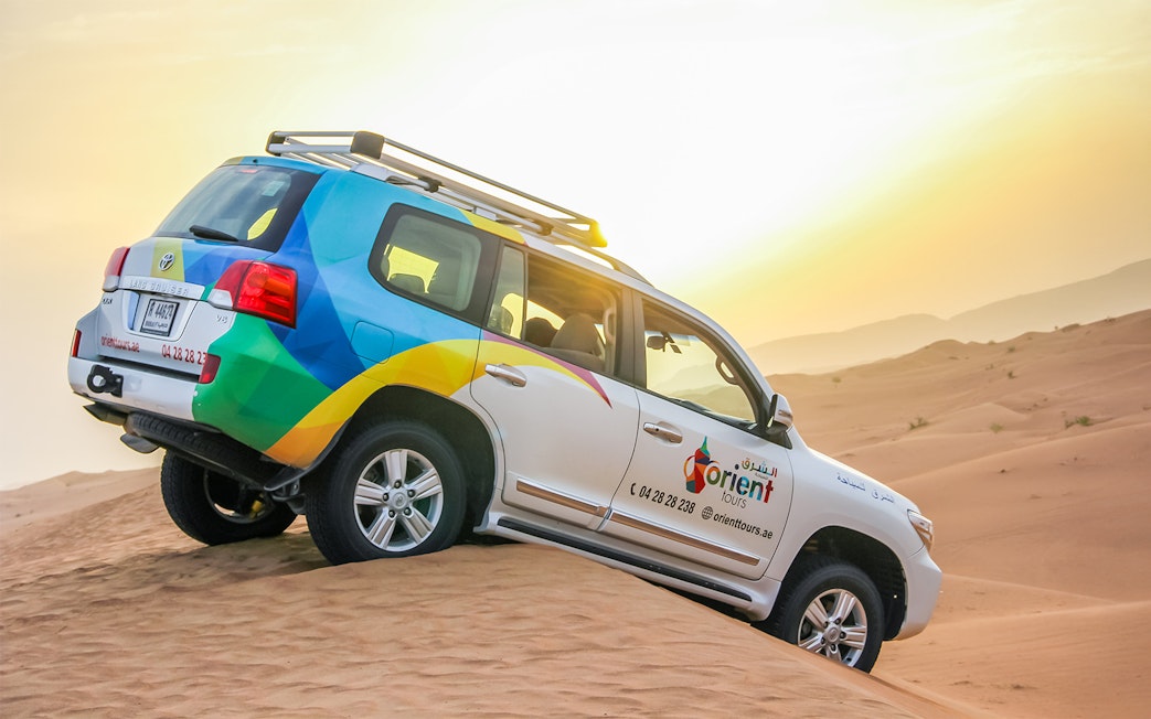 SUV driving on sand dunes during sunrise desert safari.