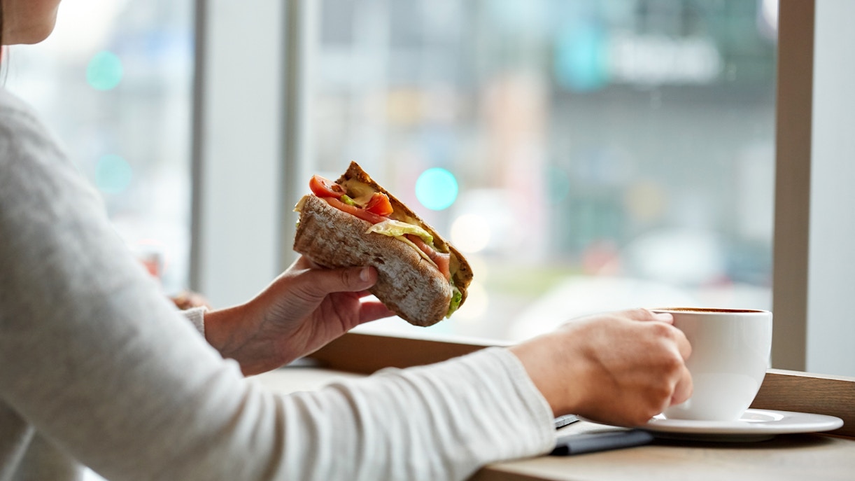 Tourist enjoying a sandwich at a Parisian café, Eiffel Tower visible in the background.