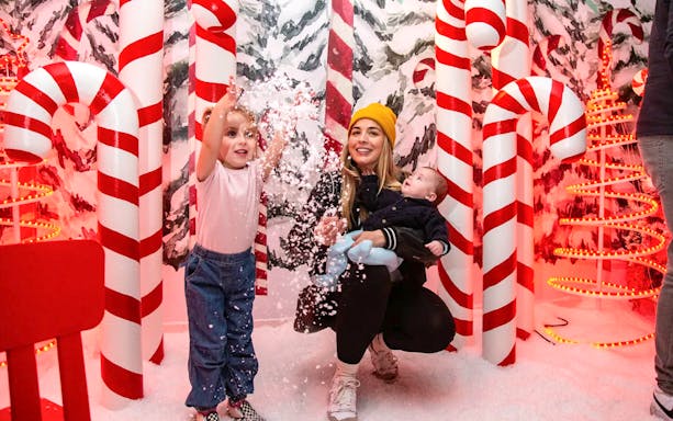 Mom and child playing with snow among large candy cane decorations.