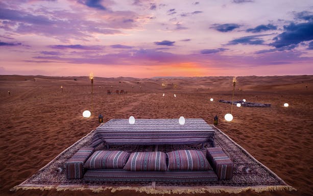 Mleiha desert lounge setup at sunset with cushions and lanterns.