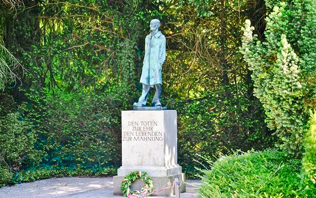 Statue and memorial at Dachau Concentration Camp surrounded by greenery.