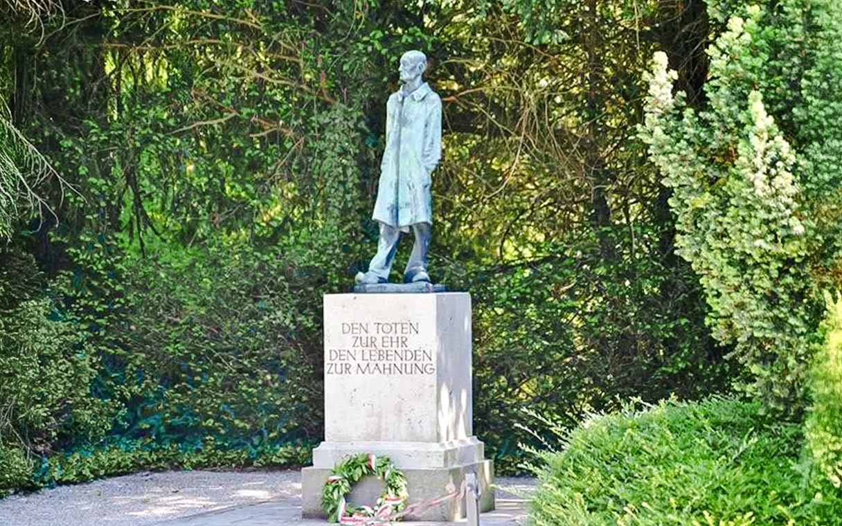 Statue and memorial at Dachau Concentration Camp surrounded by greenery.