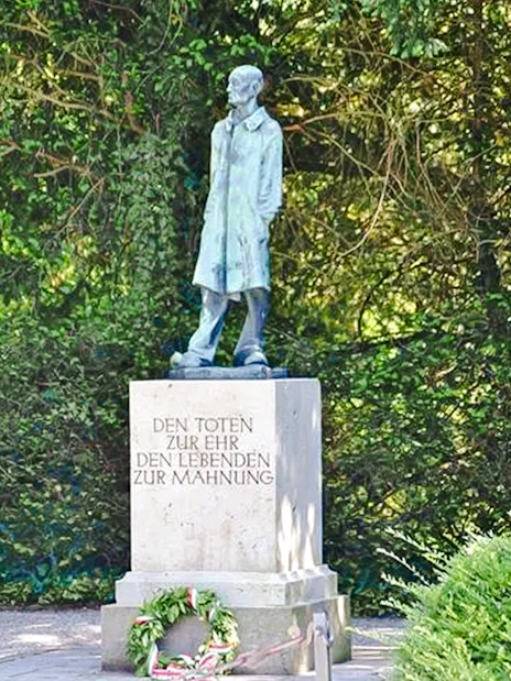 Statue and memorial at Dachau Concentration Camp surrounded by greenery.