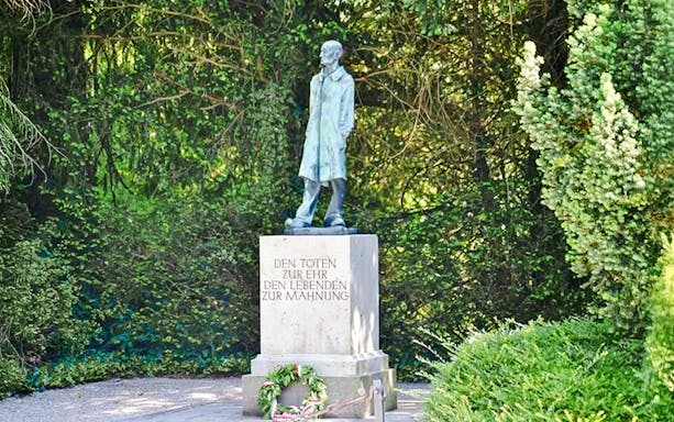 Statue and memorial at Dachau Concentration Camp surrounded by greenery.