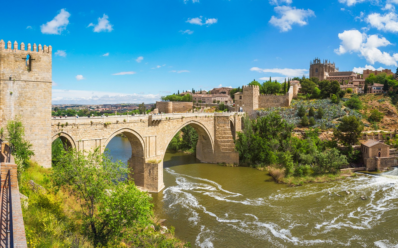 Puente de San Martin spanning the River Tagus in Toledo, Spain, with historic buildings nearby.
