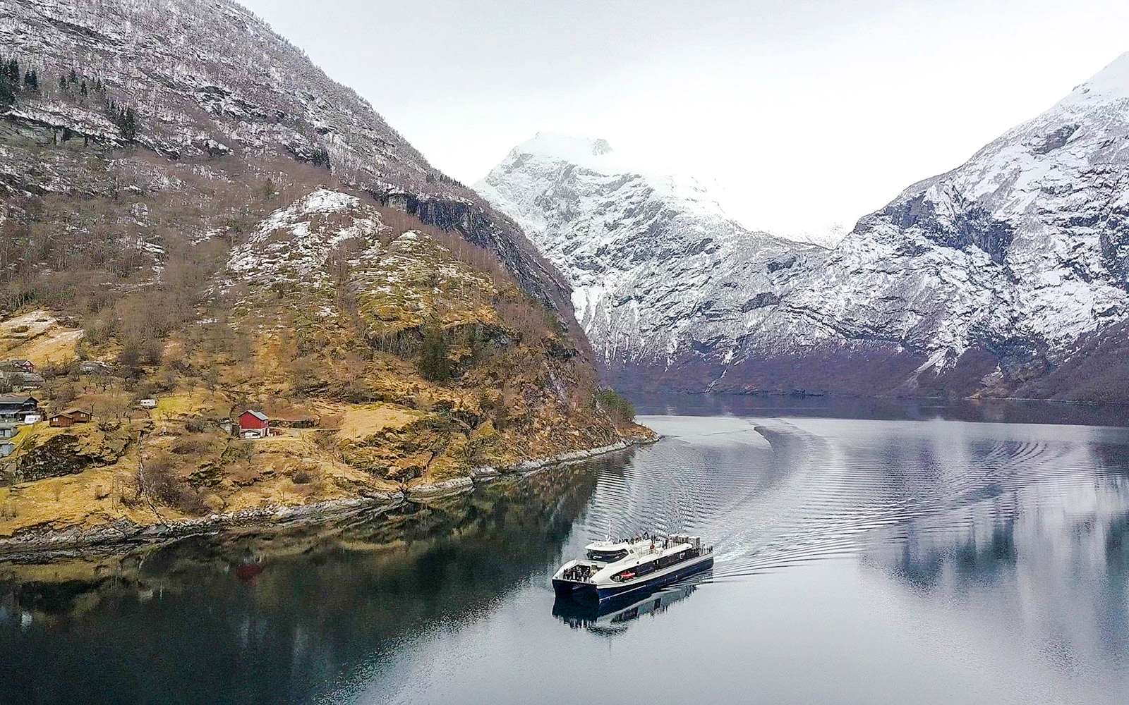 Cruise ship sailing through snow-capped fjords in Alesund, Norway.