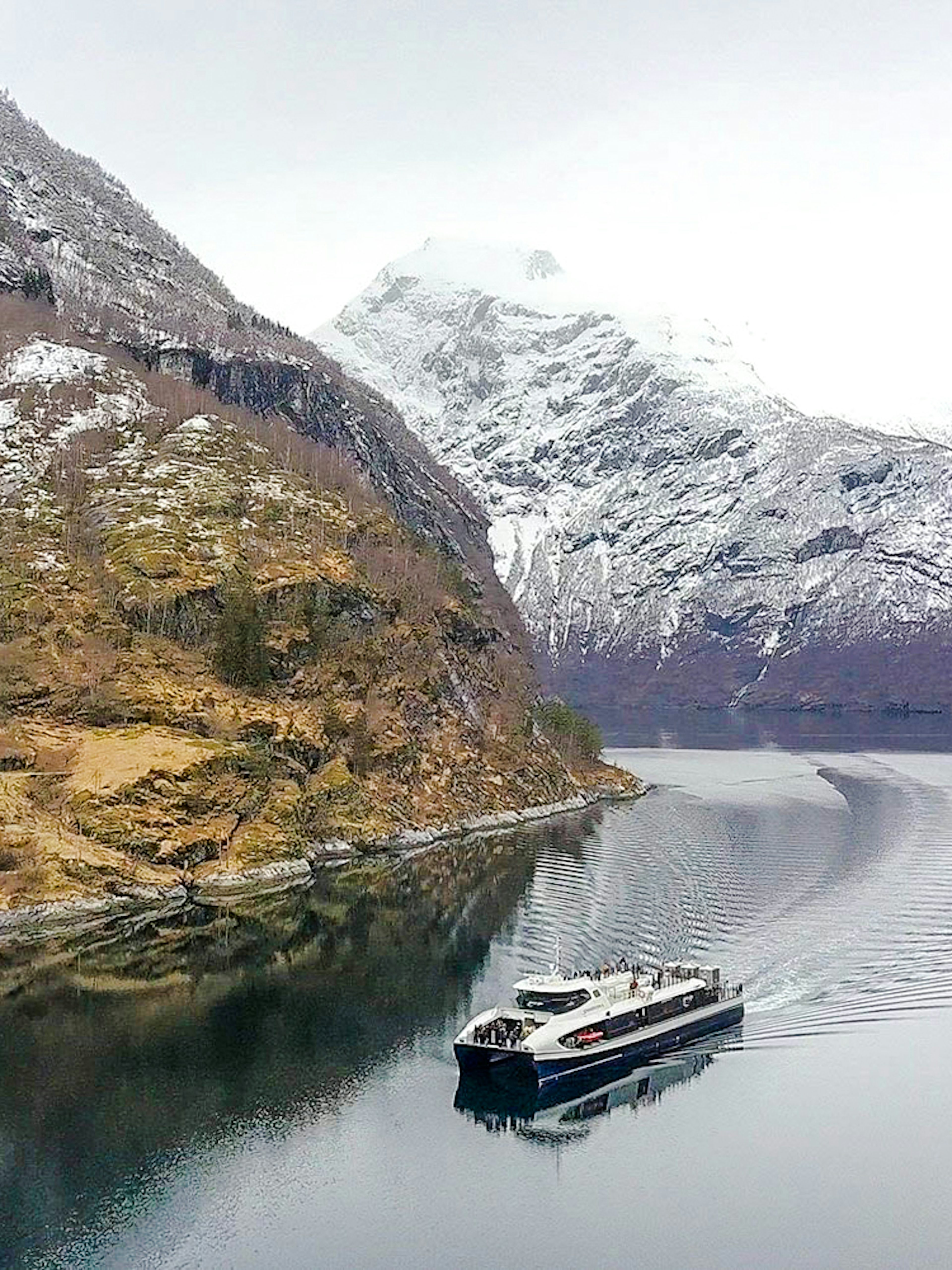 Cruise ship sailing through snow-capped fjords in Alesund, Norway.