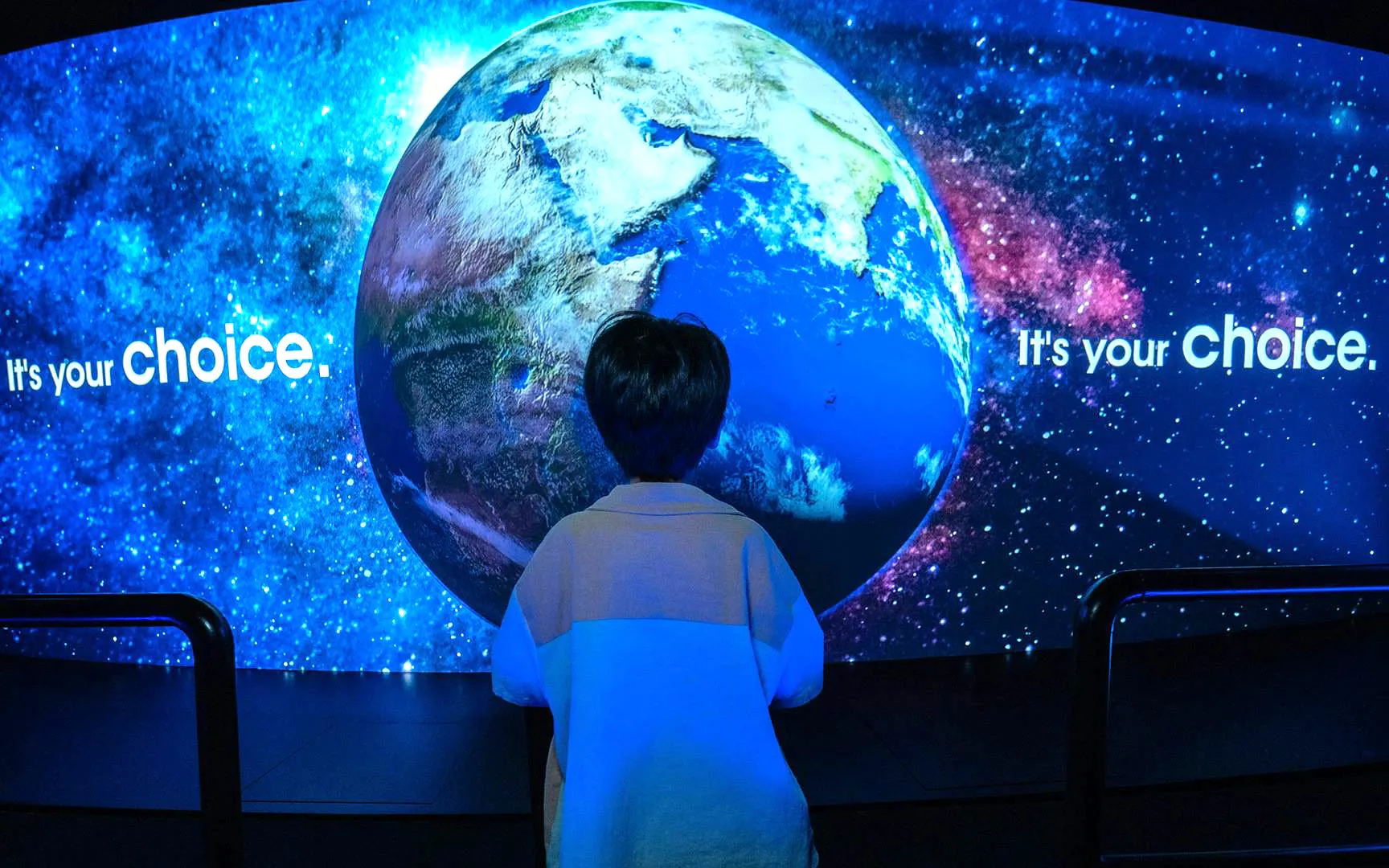 Child viewing Earth projection with "It's your choice" text, promoting Better World Better Future theme.