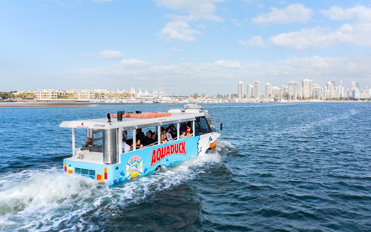 Aquaduck tour vehicle cruising on a river with city skyline in the background.