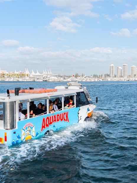 Aquaduck tour vehicle cruising on a river with city skyline in the background.