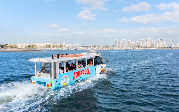 Aquaduck tour vehicle cruising on a river with city skyline in the background.