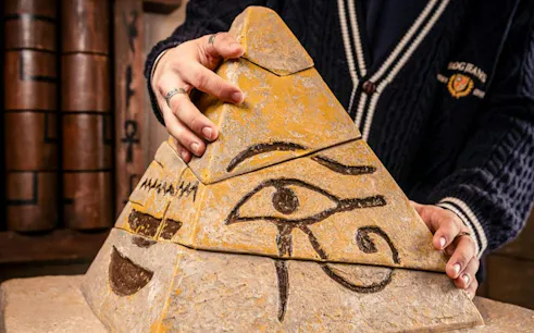 Hands adjusting a pyramid puzzle piece with Egyptian symbols in the Curse of the Pharaoh Escape Room, Dubai.