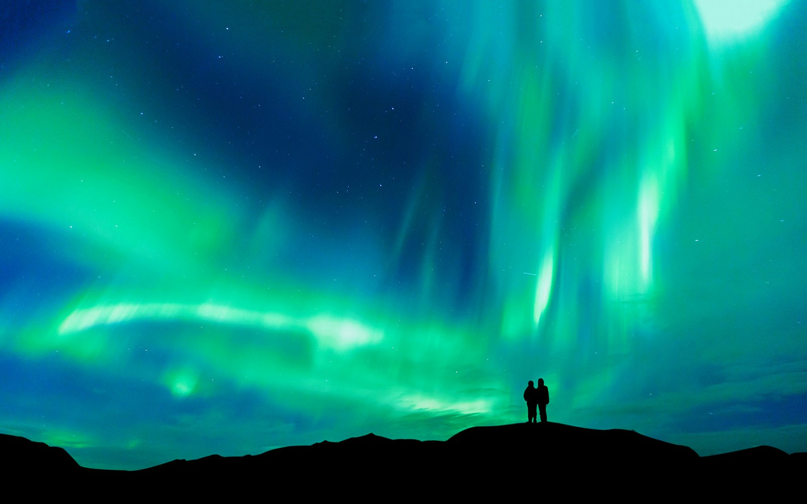 Silhouette of couple under aurora borealis on Kätkävaara Hill, Finland.