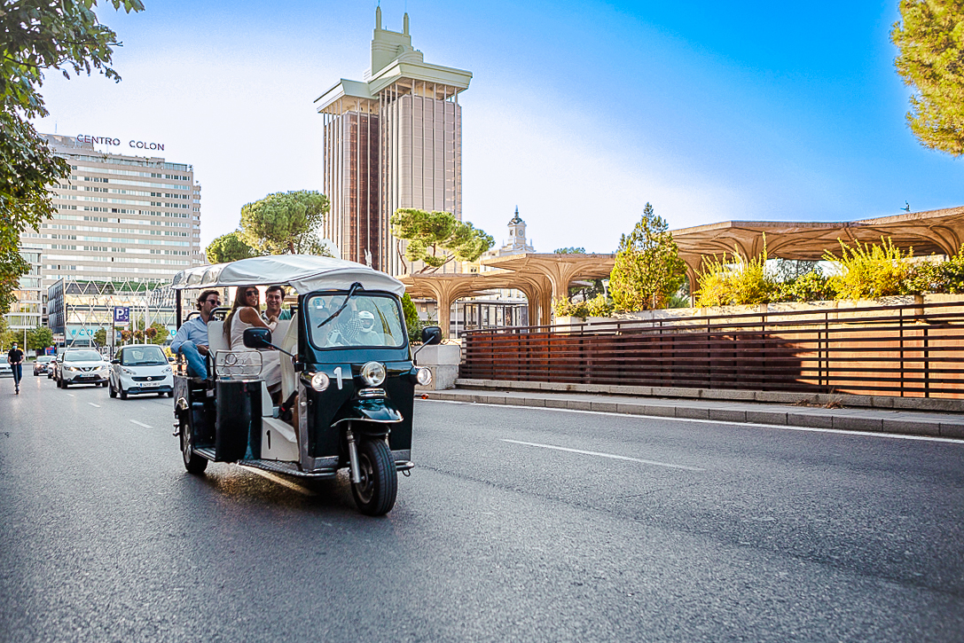 Eco Tuk Tuk driving through Madrid city street with modern buildings in the background.