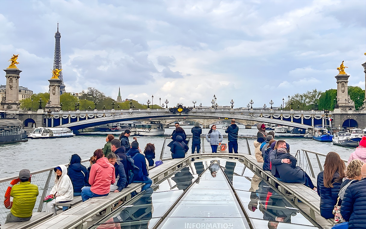 Tourists on a Seine River cruise with Eiffel Tower and Pont Alexandre III in Paris.