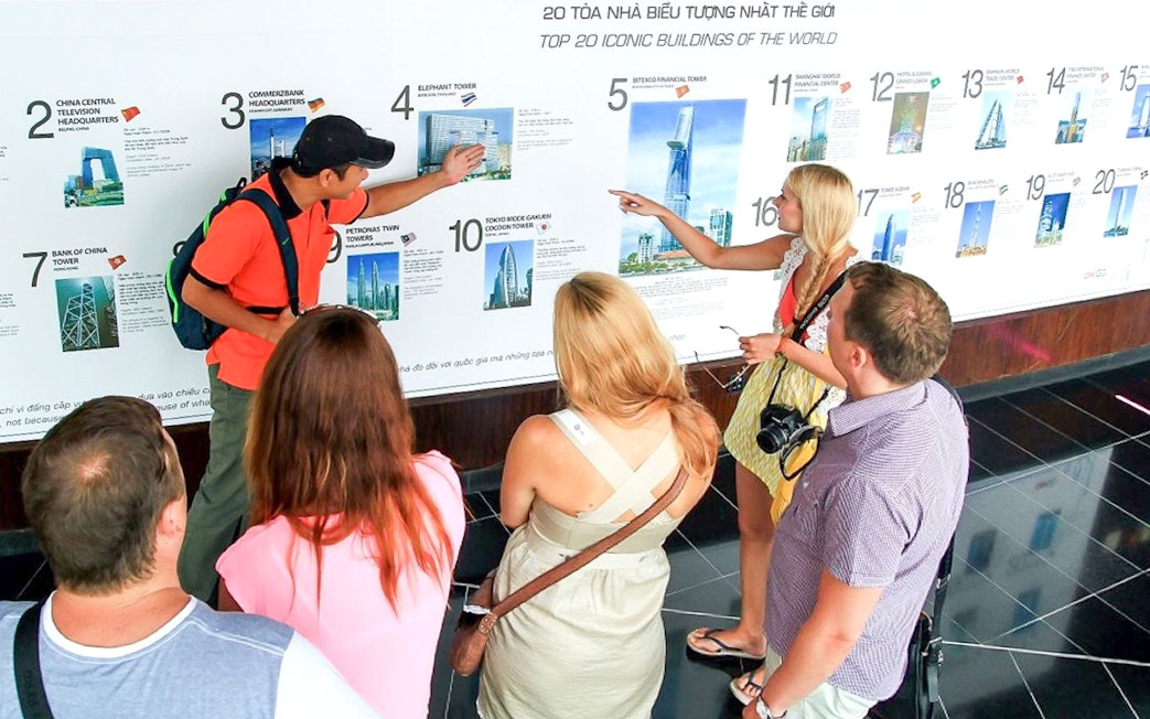 Group of tourists learning about Bitexco Financial Tower at Saigon Skydeck exhibit.