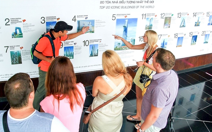 Group of tourists learning about Bitexco Financial Tower at Saigon Skydeck exhibit.