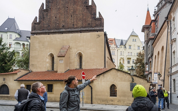 Tour guide leading guests through the Jewish Quarters in Prague, pointing at historical buildings.