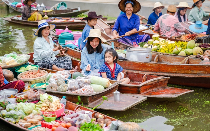 Asian tourists in boats at a floating market selling fresh produce in Thailand.