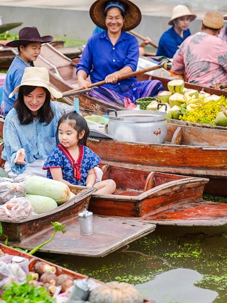 Asian tourists in boats at a floating market selling fresh produce in Thailand.