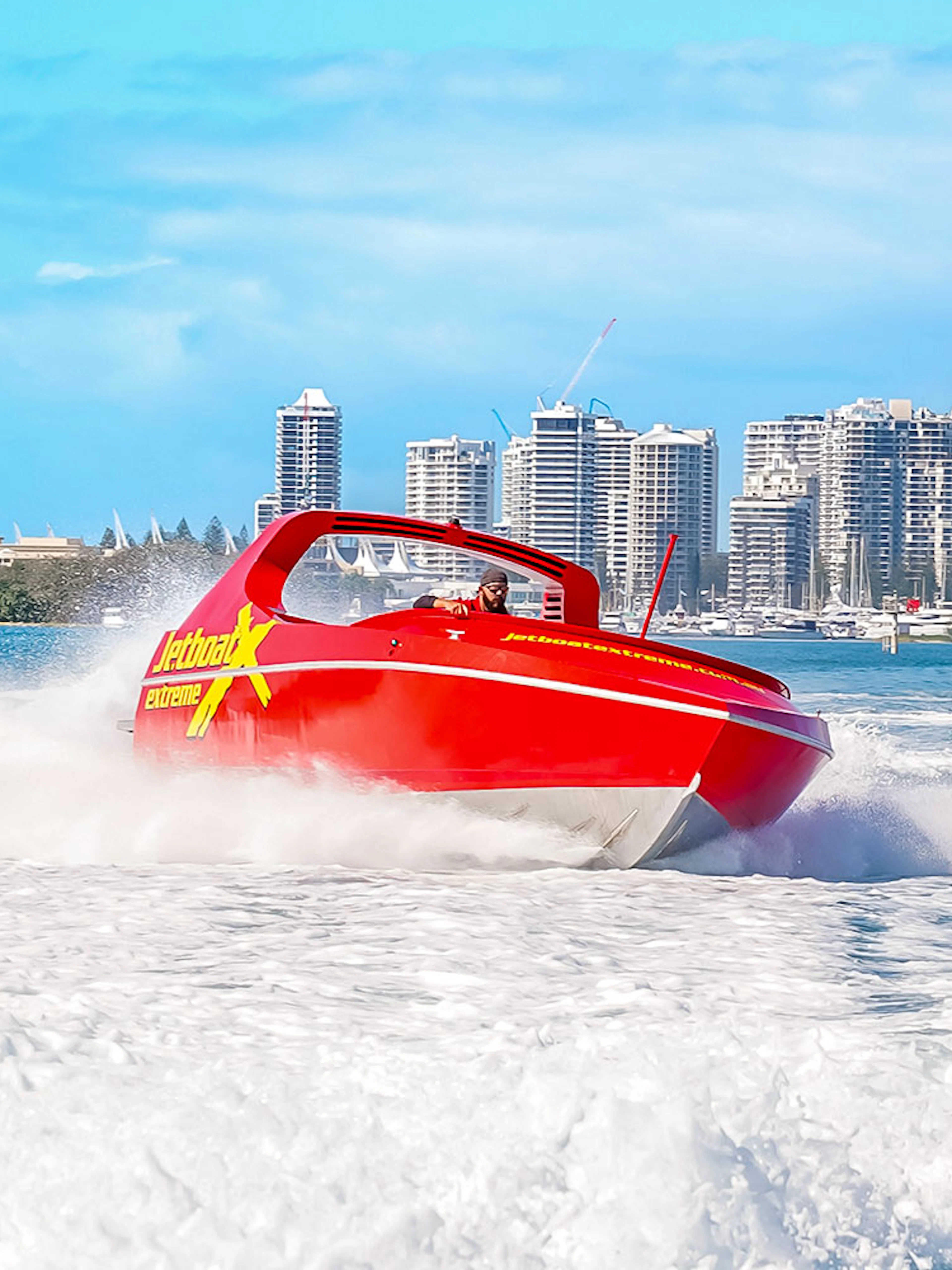Jet boat speeding on water with city skyline in the background, Ultimate Jet Boat Ride.
