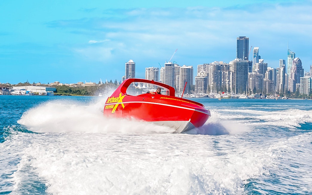 Jet boat speeding on water with city skyline in the background, Ultimate Jet Boat Ride.