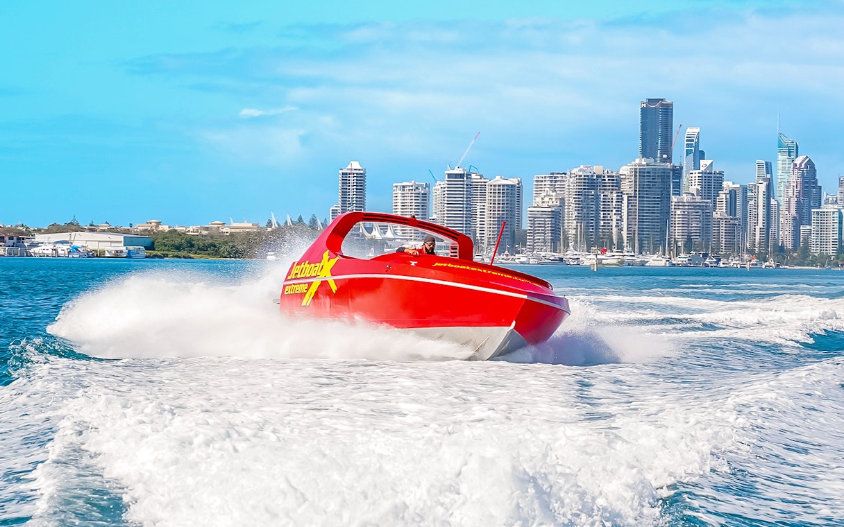 Jet boat speeding on water with city skyline in the background, Ultimate Jet Boat Ride.