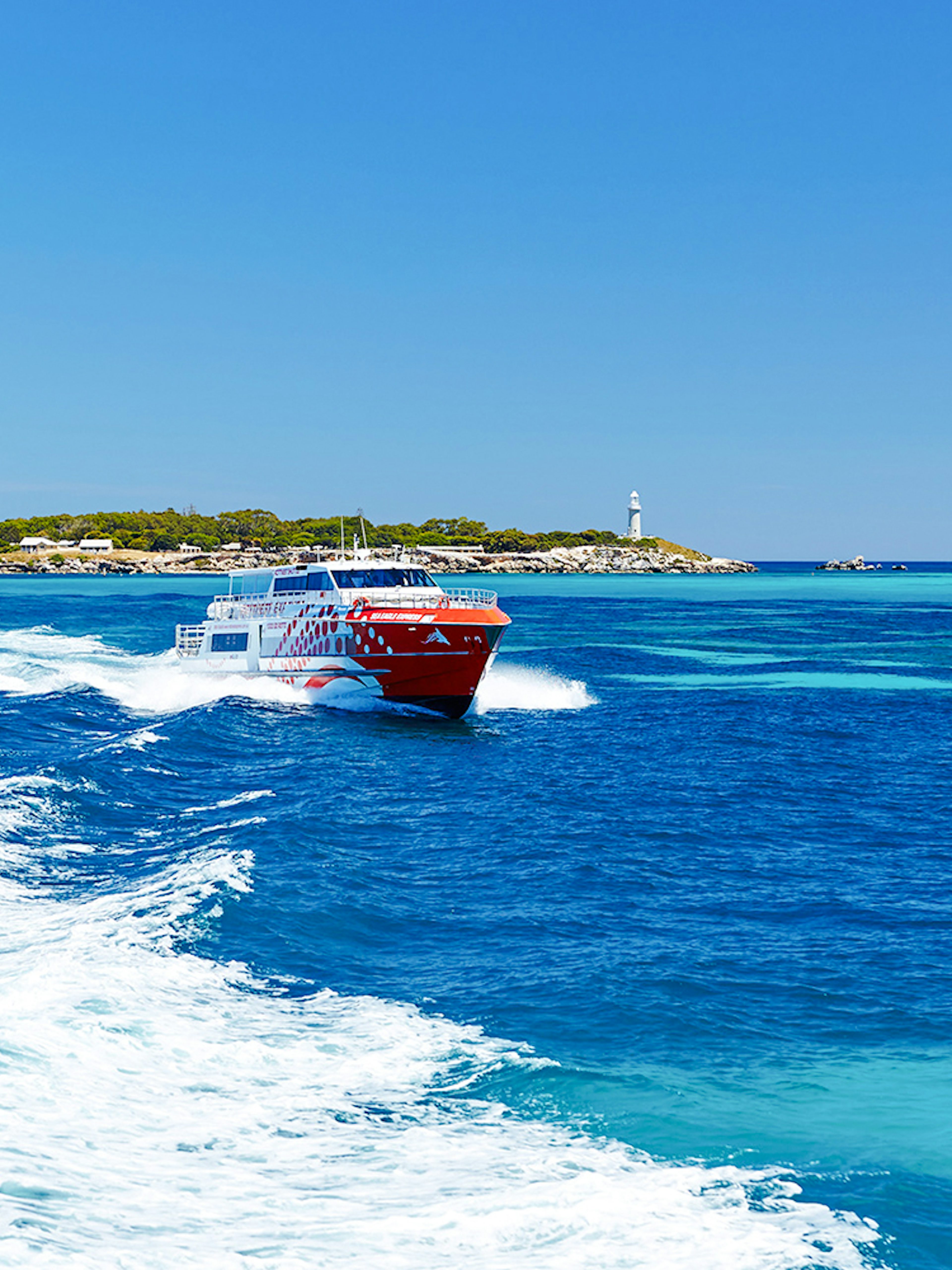 Rottnest Express ferry creating a wake, with Rottnest Island and lighthouse visible in the distance.