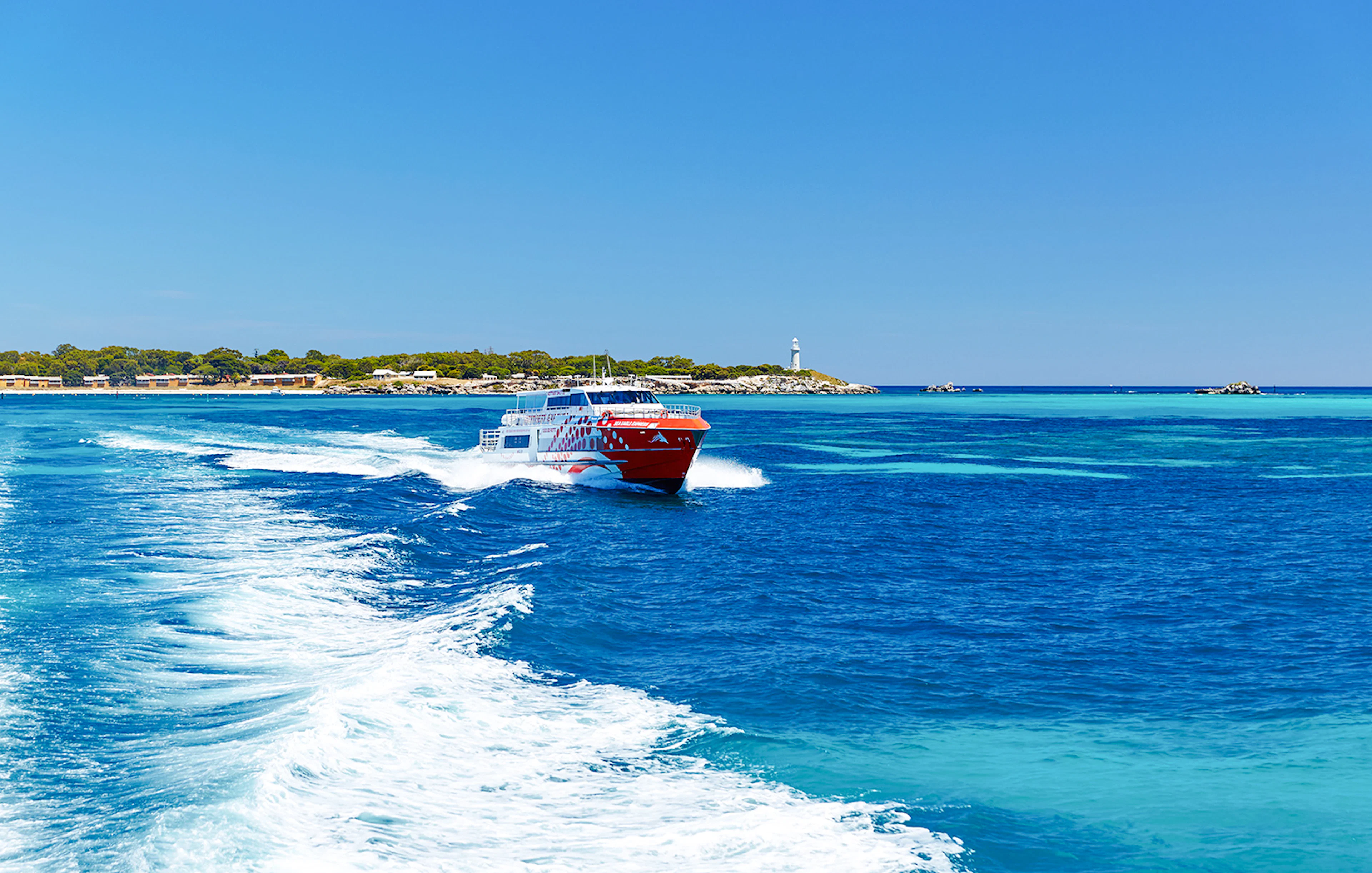 Rottnest Express ferry creating a wake, with Rottnest Island and lighthouse visible in the distance.