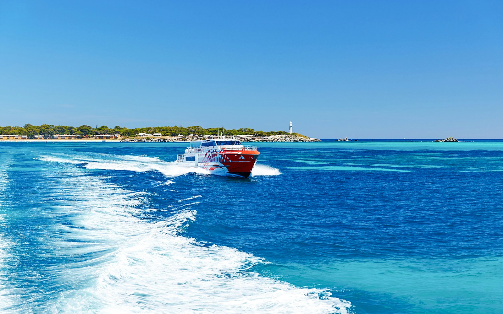 Rottnest Express ferry creating a wake, with Rottnest Island and lighthouse visible in the distance.