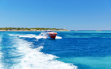 Rottnest Express ferry creating a wake, with Rottnest Island and lighthouse visible in the distance.