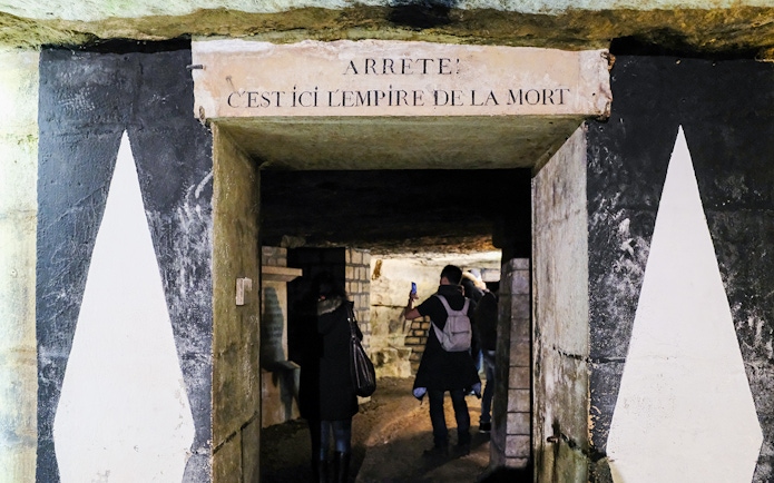 Visitors exploring the entrance of the Paris Catacombs with a sign above.