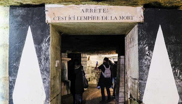 Visitors exploring the entrance of the Paris Catacombs with a sign above.