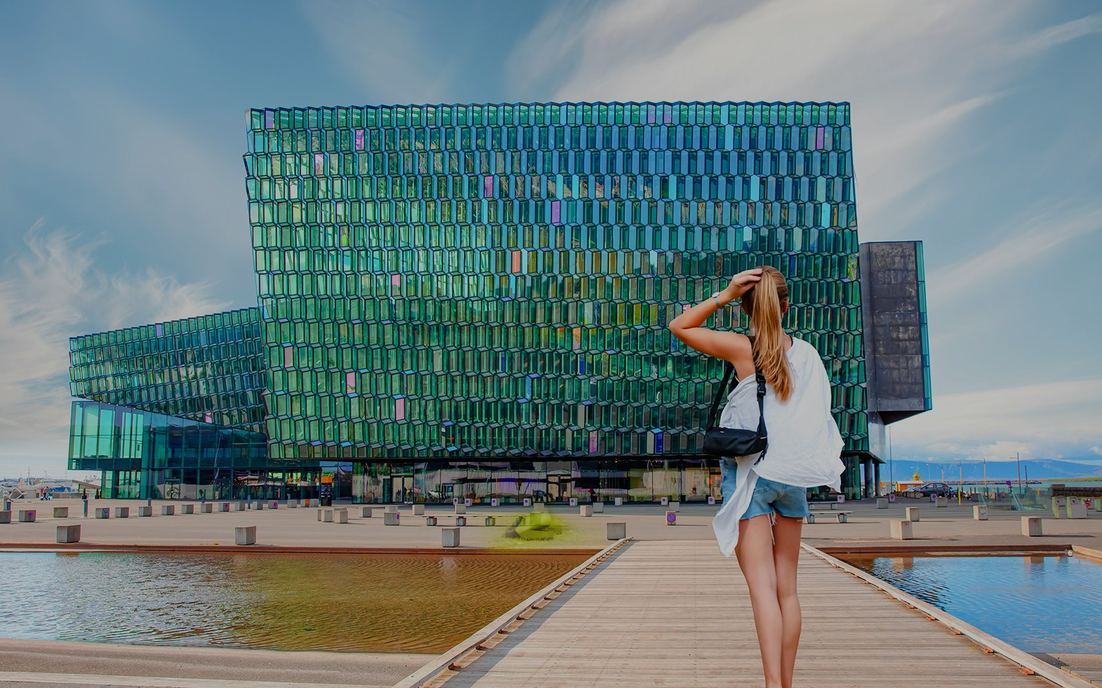 Harpa Concert Hall in Reykjavik, Iceland, with a visitor standing on the boardwalk.