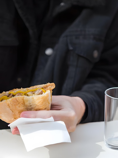 Person adding mustard to a Bifana sandwich in Lisbon.