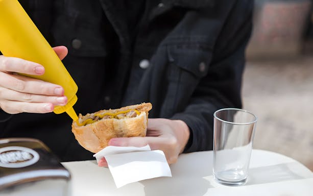 Person adding mustard to a Bifana sandwich in Lisbon.