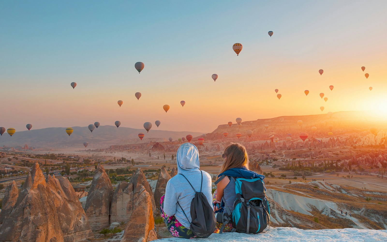Hot air balloons over Cappadocia landscape at sunrise with two people watching.
